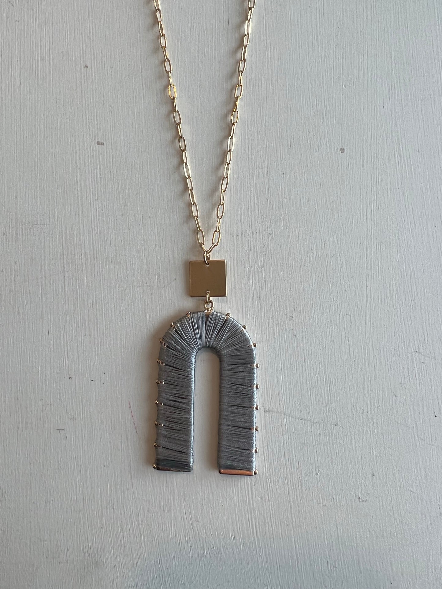An upside down U shape charm with a gold chain. 32" necklace.