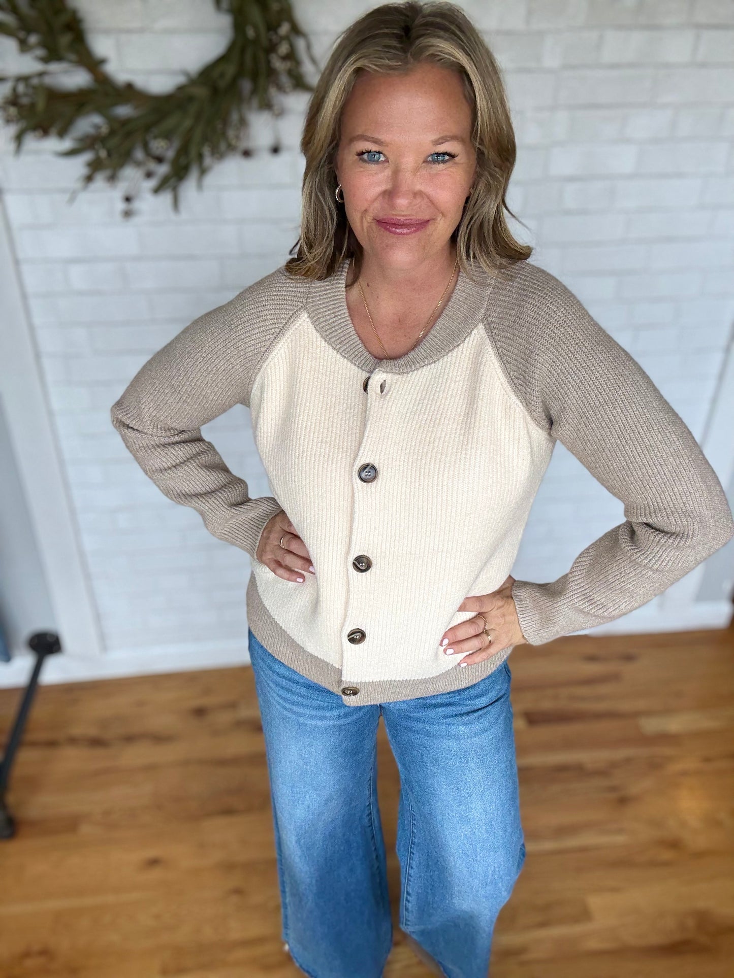 Woman wearing a beige and white sweater with button details, standing indoors.